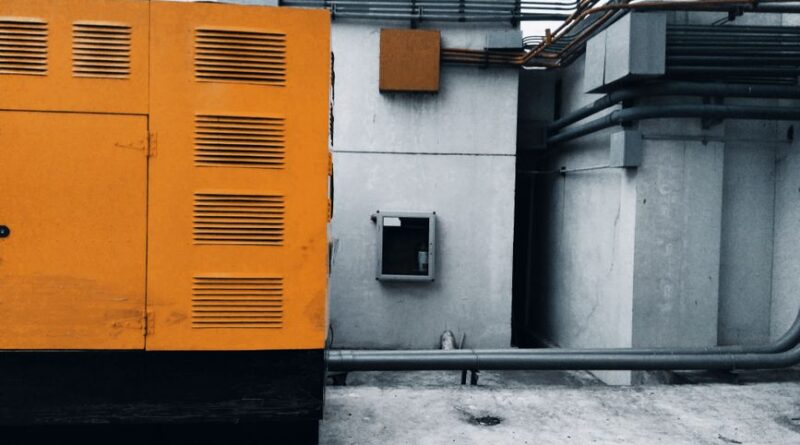 Outdoor view of an industrial generator with visible piping and wiring against a concrete wall. - Photo by ezrah lane on Pexels